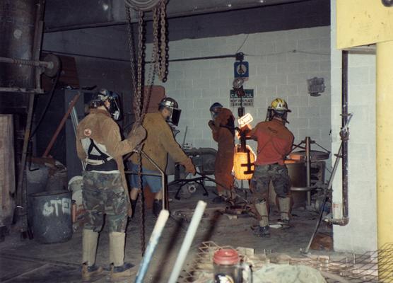 Scott Oberlink, Jack Gron, an unidentified man and Andrew Marsh lifting a crucible out of the furnace at the University of Kentucky foundry for the casting of 