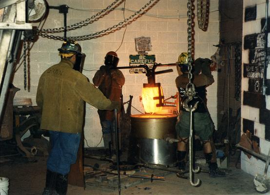 Jack Gron, an unidentified man and Andrew Marsh lifting a crucible out of the furnace at the University of Kentucky foundry for the casting of 