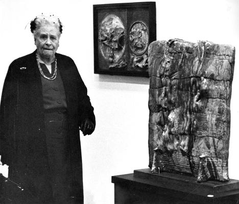 A woman next to a ceramic pouch vessel in an exhibit entitled 