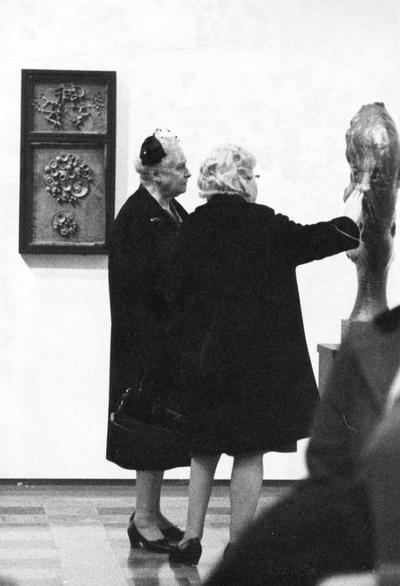 Two women viewing a ceramic vessel at an exhibit entitled 