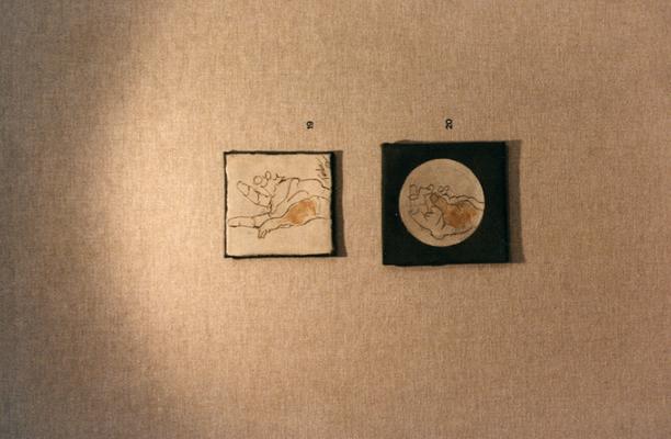 Two clay tile drawings of hands in an exhibit entitled 
