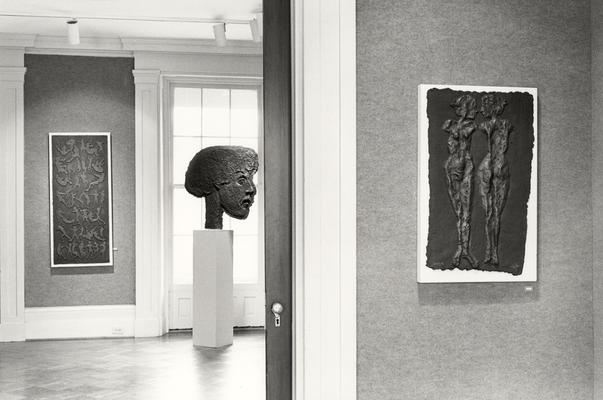 Three cast paper sculptures of human figures, one shaped as a large head, in an exhibit entitled 