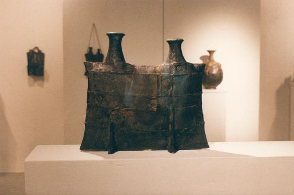 An image of a ceramic pouch vessel and three other vessels in the background in the 