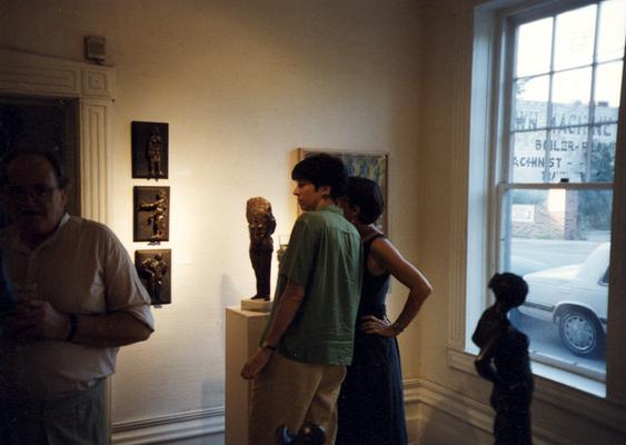A image of John Tuska, Debra Hensley and an unidentified person viewing artwork at the Heike Pickett Gallery