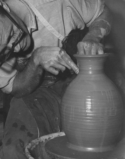 An image John Tuska shaping the rim of a clay pot on a potter's wheel