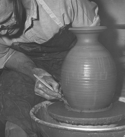 An image John Tuska trimming the base of a clay pot on a potter's wheel
