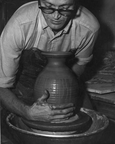 An image John Tuska lifting a clay pot from a potter's wheel
