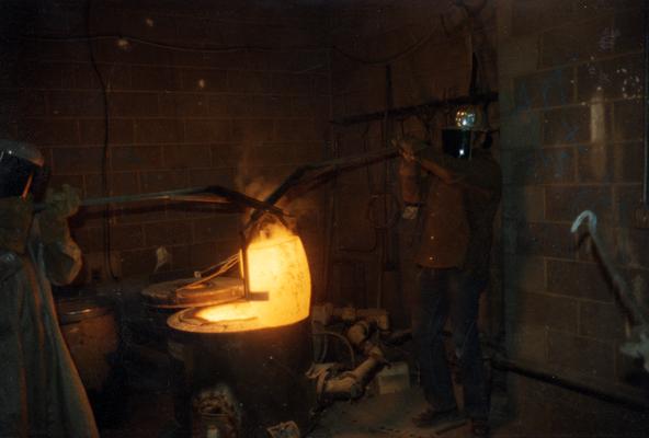 Jack Gron and John Tuska lifting a crucible out of the furnace in the University of Kentucky foundry. The photograph was taken by Zig Gierlach