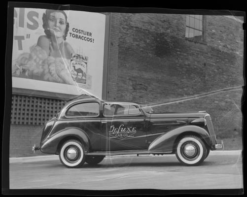 Deluxe Cab Company, 506 West Main; Deluxe Cab car parked in front of tobacco ad on exterior of building