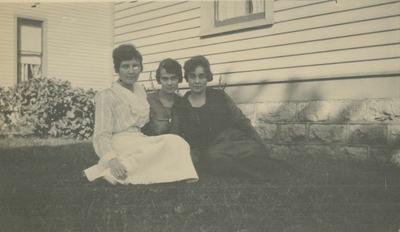 3 women sitting on the grass with houses in the background