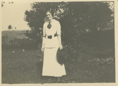 a woman standing outside holding her hat and a flower