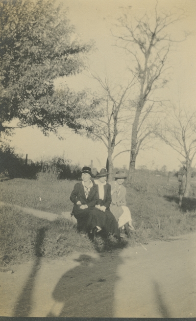 3 women sitting on the grass next to the road