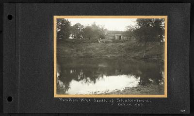 Dilapidated wooden building with fallen wooden fencing in front on bank of small pond, notation                          Pondon Pike South of Shakertown Oct. 14. 1906