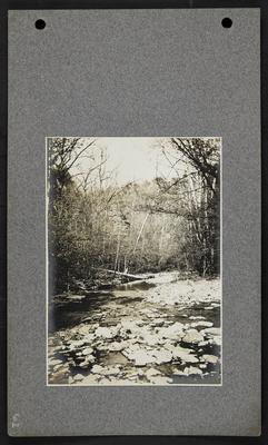 Small river with many rocks along edge, bluffs rising in distance