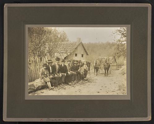 Unidentified males sitting on a log, on the dirt road is a horse drawn buggy and two males. The photograph was printed in Louisa, Kentucky. The bottom of the photograph reads: Twenty-three notches in his gun