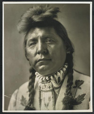 Formal portrait of a man wearing traditional Native American dress. The back of the photograph identifies him as: Fish Wolf Robe