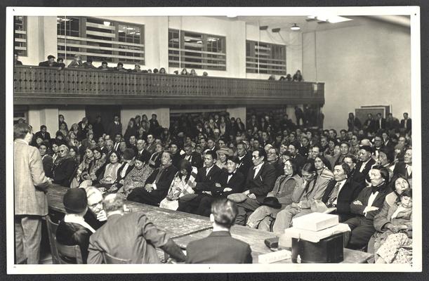 A group of Native Americans sitting in an assebly in a gymnasium. Back of the photograph reads: Assembly March 22, 1931. Illiteracy Clinic. Blackfeet Indian Reservation