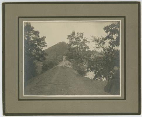 A dirt road, back of the photograph reads: The Mountain Child- His Environment. Road up the hill two miles to the school. Getting an education in the mountains is 'up hill business' anyways