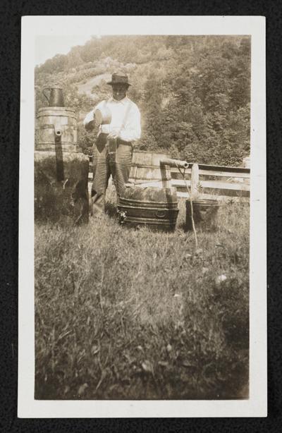 Unidentified male with a moonshine still. The back of the photograph reads: This still is made of two wash tubs, two barrels, one gasoline tank, one lard tub. The worms are made of wood