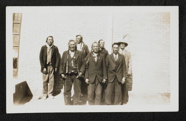 Group of 7 men. The back of the photograph reads: Front Row- Mike Short Man, Judge Bird Rattler, Rides on the Door. Back Row- Three Calfs, John Shoots First, Louie Champagne, Dick Kipp