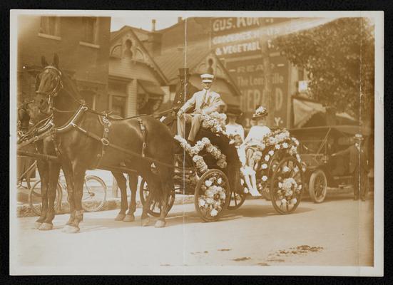 Group, unidentified, sitting in a carriage drawn by two horses, decorated with flowers