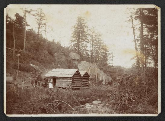 Unidentified family in front of a log cabin, back of the photograph reads: Screen No. 2- The Mountain Child- His Environment. Picture No. 14: And having all these- he may yet be poor of the goddess Minerva, tarries too long, for not knowing the value of his possessions he will sell his birth right to foreign syndicate for a mess of pottige