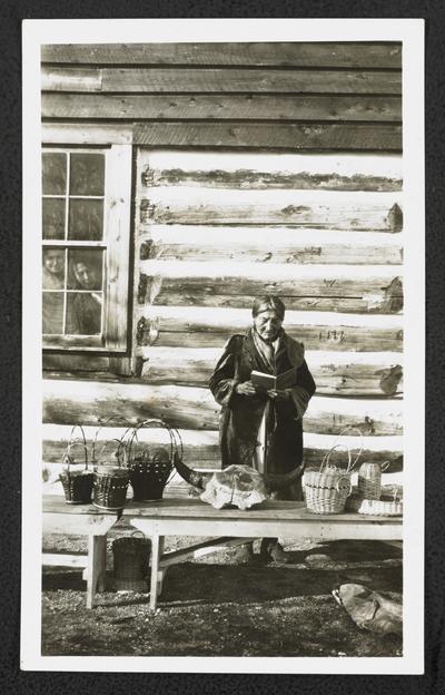 Two women looking out a window at a woman reading a book, standing in front of a display table. Back of the photograph identifies her as: Mrs. Blackbull age 72