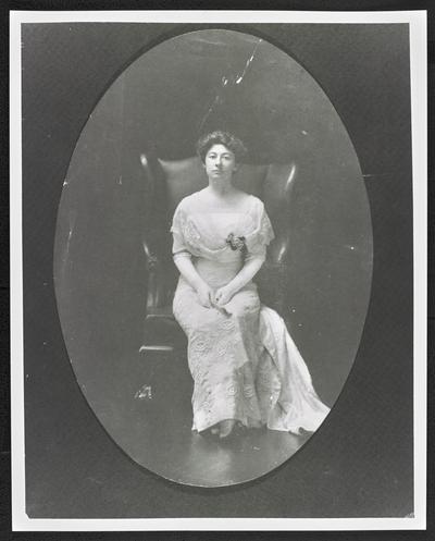 Full-length formal portrait of Cora Wilson Stewart, wearing a white dress and gloves, sitting in a leather chair