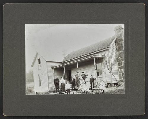 Family, unidentified, standing in front of a wooden house