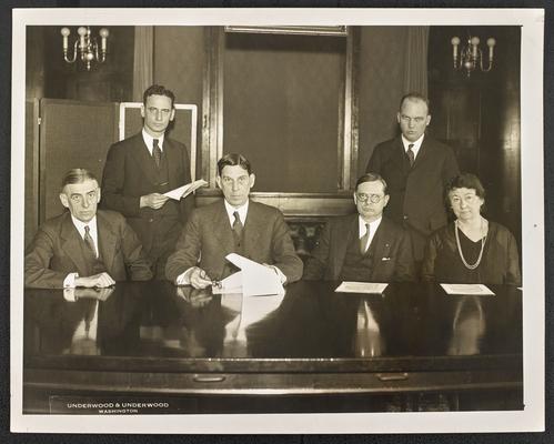 Cora Wilson Stewart as an older woman, seated at a table with 3 unidentified men, 2 more men standing behind them. The bottom of the photograph reads: Underwood & Underwood, Washington