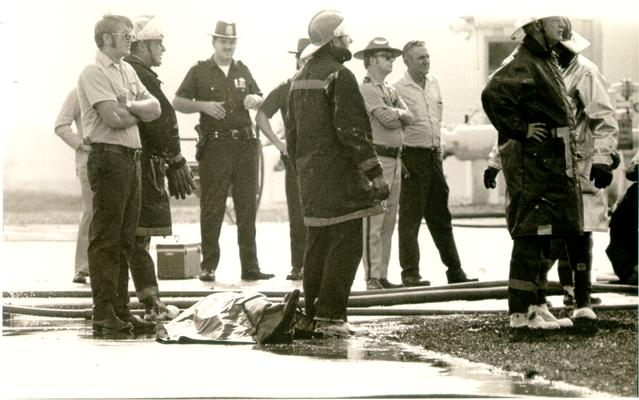 Ashland Bulk Oil Plant; 1973 Explosion and Fire; Firemen and authorities stand near body of one of the dead