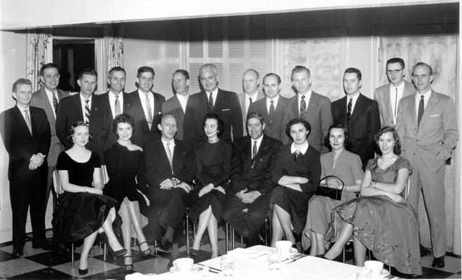 Groups; Unidentified; A group of men and women gathered next to a dinner table