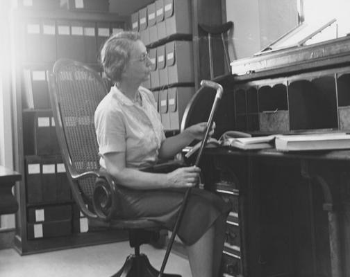 Cooper, Mary Hester, born 1904, died 1987, University Archivist 1956 - 1970, pictured seated at University President James K. Patterson's desk looking over biographies of Patterson, Public Relations Department