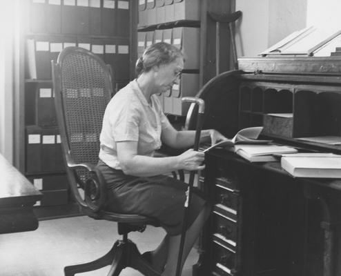 Cooper, Mary Hester, born 1904, died 1987, University Archivist 1956 - 1970, pictured seated at University President James K. Patterson's desk looking over biographies of Patterson, Public Relations Department