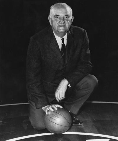 Rupp, Adolph, University of Kentucky Basketball Coach 1930-1971, pictured posting at center court of Memorial Colleseum with basketball
