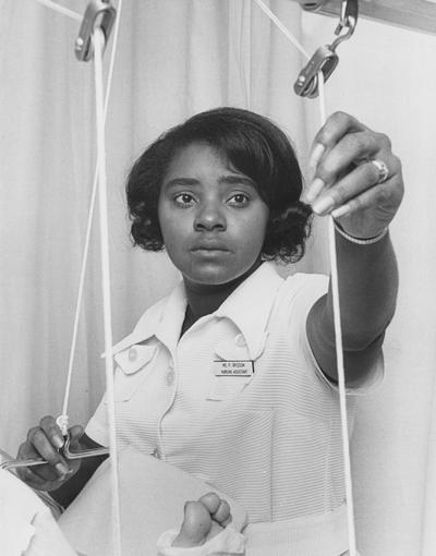 Grissom, P., an African - American nursing assistant, is helping a patient in the Medical Center