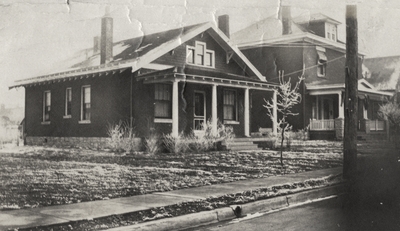 An image of a one and a half story house (same house as in image 16) in the foreground and a two and a half story house in the background. This image was found pasted on the back of page 100 of 