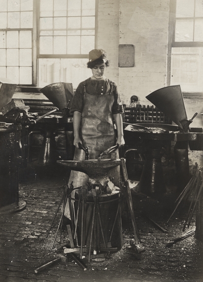 A portrait of Margaret Ingels standing behind a forge preparing to work on metal. This image was found pasted on the front of page 102 of 