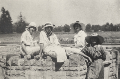 A portrait of four unidentified women sitting and leaning on a stone wall. This image was found pasted on the front of page 100 of 