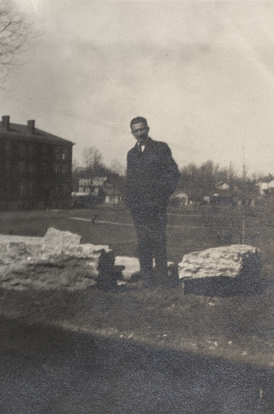 An image of an unidentified man standing next to large rocks and above a field. This image was found pasted on the front of page 103 of 