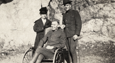 A portrait taken outside of two unidentified men in military uniforms and an unidentified woman (the woman may be Margaret Ingels' mother). One of the men has a cane and the other is sitting in a wheel chair. Taken by De Lure Studio, Hot Springs, Arkansas. This print was found pasted to the back of page 108 of 