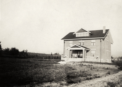 An image of a two and a half story brick house with a corn field on the left. This print was found pasted to the back of page 105 of 