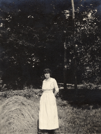 A portrait of a woman standing in a field next to a haystack and some trees. This print was found pasted to the back of page 110 of 