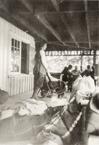 An image of group of unidentified persons sitting and standing on a porch. The back of the print is stamped 