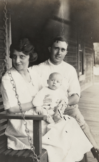 A portrait of an unidentified man, woman and baby on a porch swing. This print has a note on the back. This print was found pasted to the back of page 115 of 