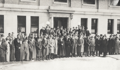 A group portrait of men and Margaret Ingels standing in front of a building. This print was found pasted to the back of page 117 of 