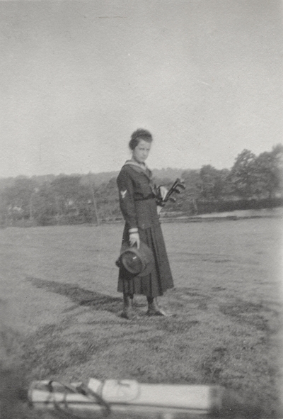 A portrait of Margaret Ingels holding golf clubs in a field. This print was found pasted to the front of page 110 of 