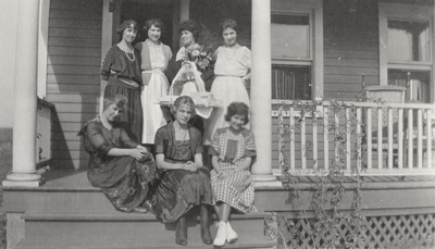 A group portrait of unidentified women sitting and standing on a porch. This print was printed by the Elizabeth Novelty Co. 923 Elizabeth, N. J. This print was found among the 