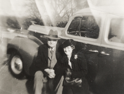 A portrait of an unidentified woman and man sitting on the floor board of a car. The car may be a 1938 Ford four door Sedan