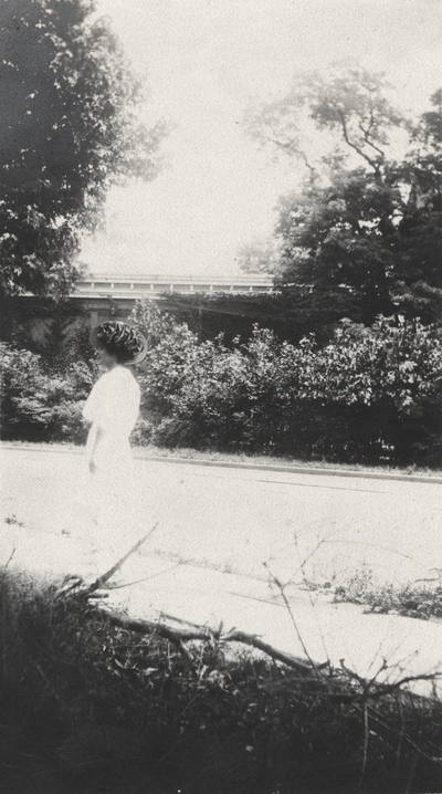 An image of an unidentified woman wearing a hat walking on a sidewalk. This print was found pasted to the front of page 104 of 
